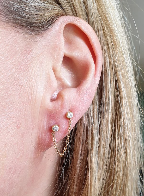 an ear lobe wearing two cz gems in gold from Anatometal with a chain hanging between the two