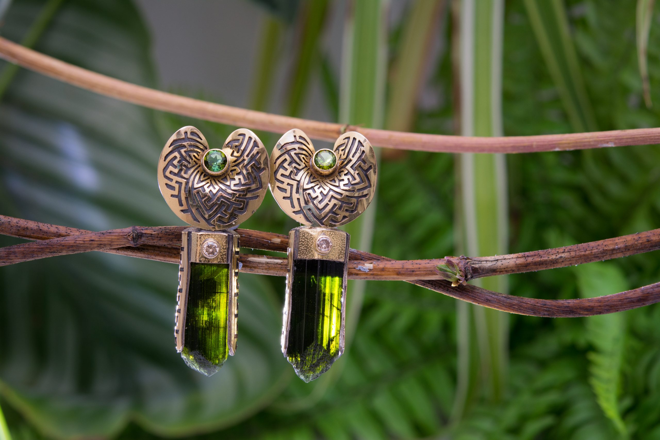 Genuine green tourmaline ear weights crafted by Naga, balanced on a branch the pair are side by side with curved silver cup shaped wearable pieces